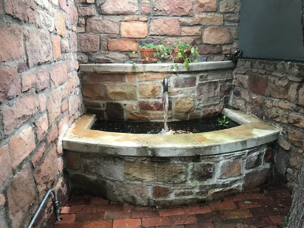 Stone wall fountain with water spilling into a basin